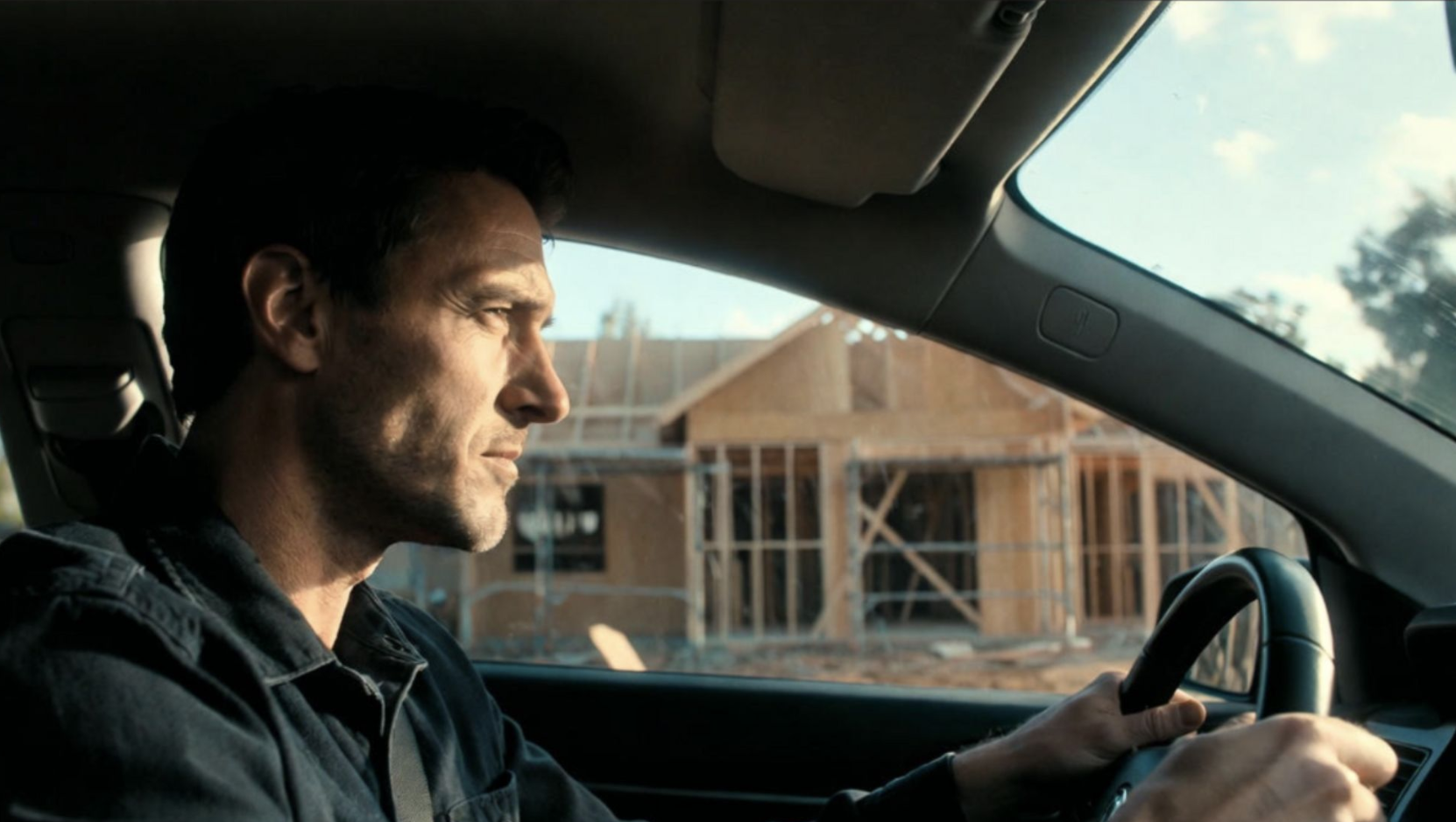 Man driving past a new home under construction during the custom home building process