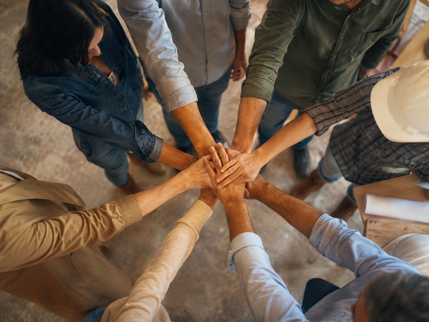Construction team and clients placing hands together in a circle to represent teamwork during a custom home project